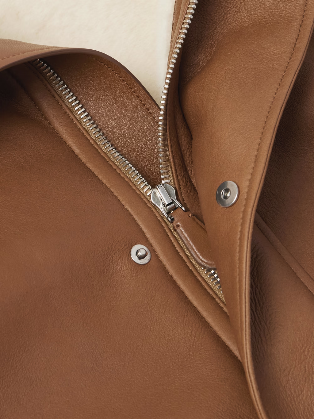 Close-up of a brown leather jacket with a zipper