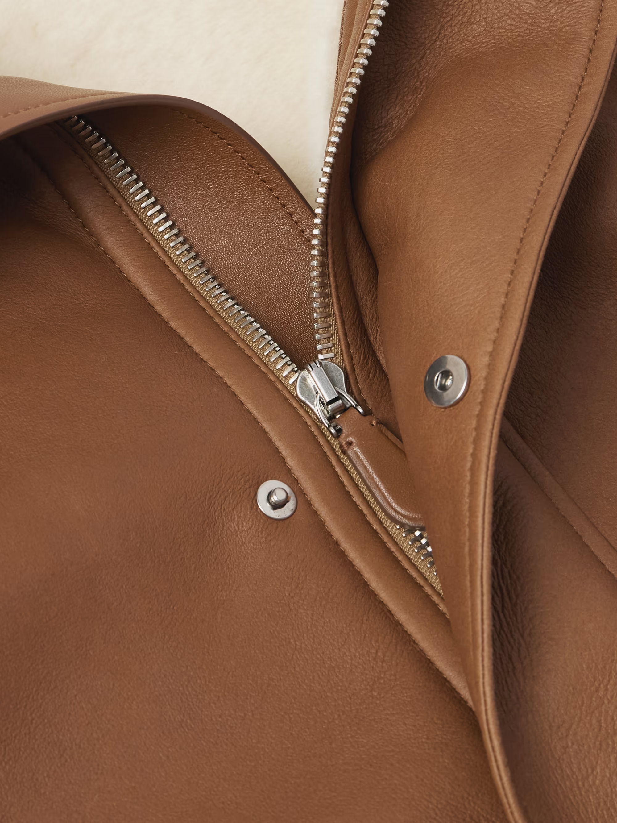 Close-up of a brown leather jacket with a zipper